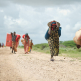 Women, walking with what possesions they can carry, arrive in a steady trickle at an IDP camp erected next to an AMISOM military base near the town of Jowhar, Somalia, on November 12. Heavy rains in Somalia, coupled with recent disputes between clans, has resulted in over four thousand IDPs seeking shelter at an AMISOM military base near the town of Jowhar, with more arriving daily. AU UN IST Photo / Tobin Jones. Original public domain image from Flickr